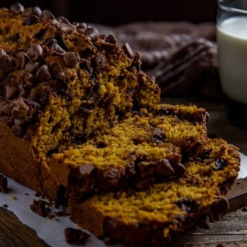 A loaf of baked bread with two slices stacked in front of it.