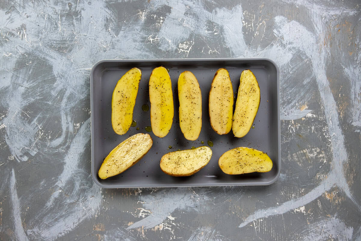 Eight raw, seasoned potato halves on a sheet pan.