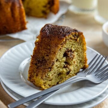 A slice of cake on top of two, stacked round white plate with two forks resting on the plate.