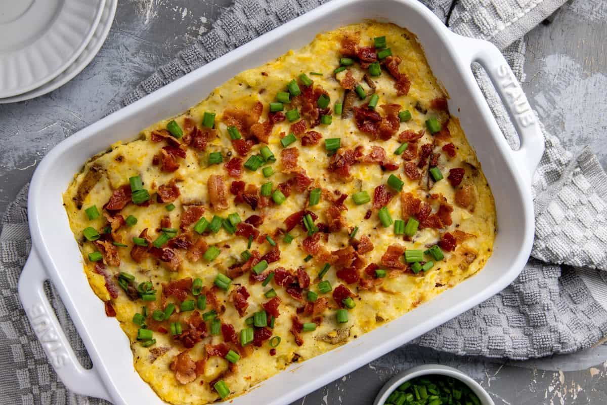 White casserole dish filled with baked mashed potatoes. Garnished with cooked crumbled bacon and sliced green onions.