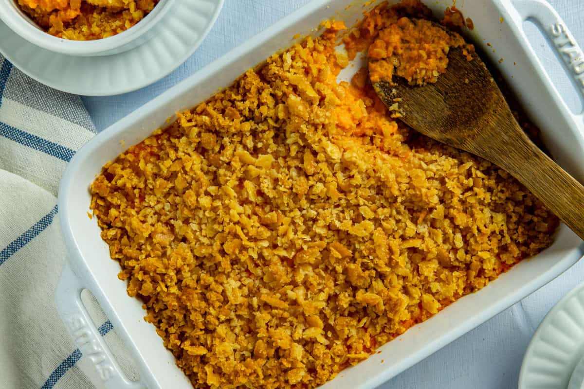 Baked carrot casserole in a white casserole dish. A wooden serving spoon is scooping out a portion.