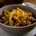 Cooked chicken chili topped with sliced green onions and corn chips.