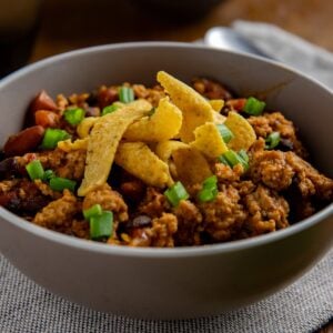 Cooked chicken chili topped with sliced green onions and corn chips.