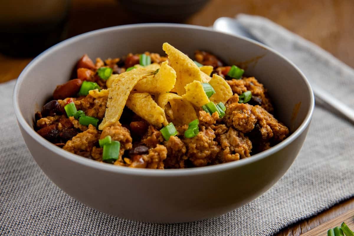 Overhead view of cooked chicken chili in a bowl topped with corn chips and sliced green onions.