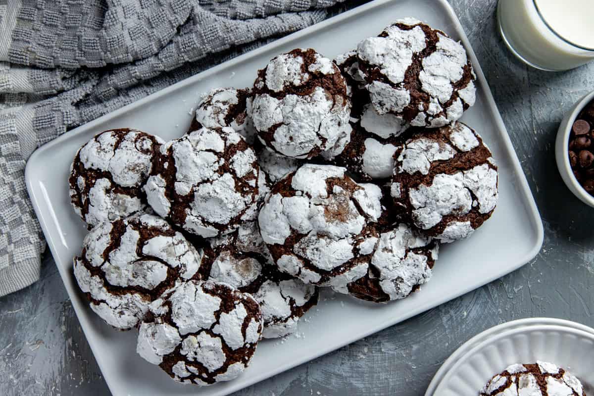 Baked cookies stacked on a white platter. Glass of milk in the background.
