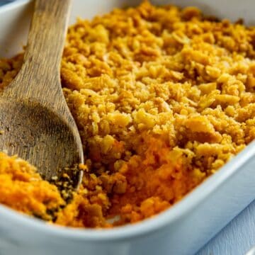 Baked carrot casserole in a white casserole dish. A wooden serving spoon is scooping out a portion.