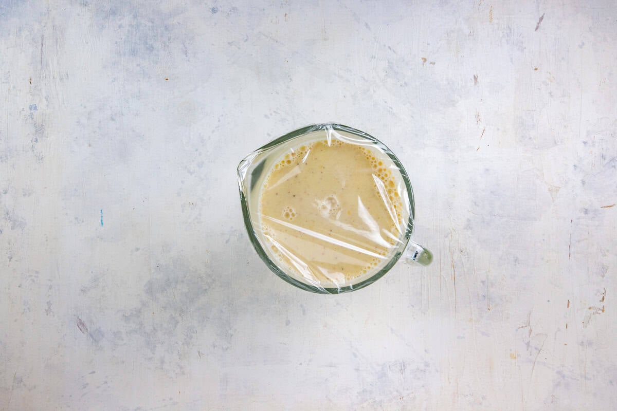 Cooled eggnog in a glass container covered with plastic wrap.