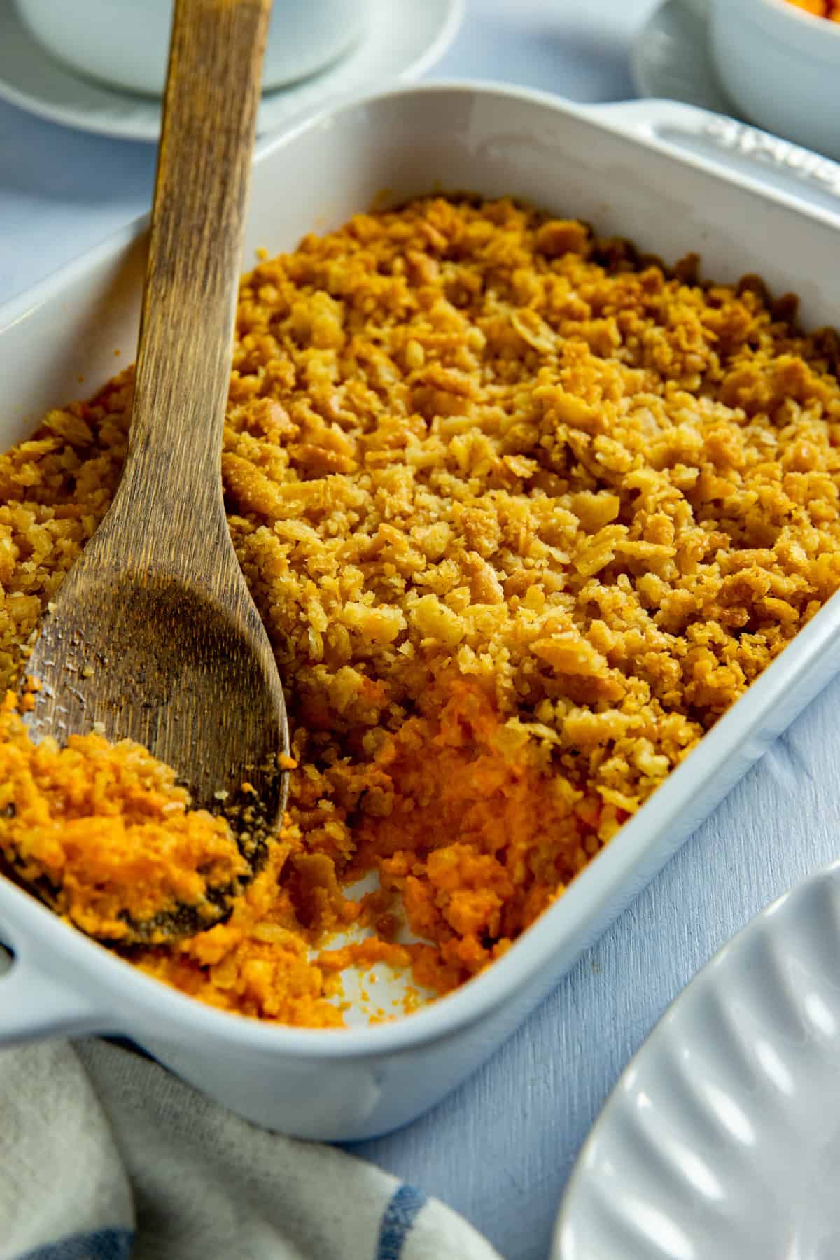 Baked carrot casserole in a white casserole dish. A wooden serving spoon is scooping out a portion.
