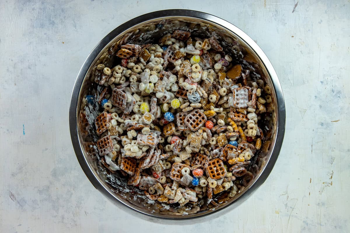 Melted almond bark mixed with the chex mix mixture in a bowl.