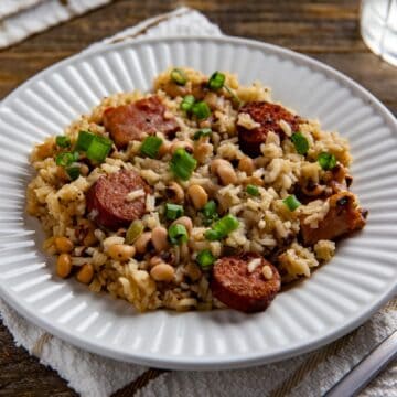 Cooked Hoppin John garnished with sliced green onions on a white plate.