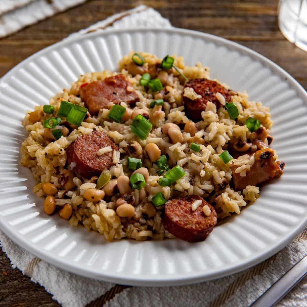 Cooked Hoppin John garnished with sliced green onions on a white plate.