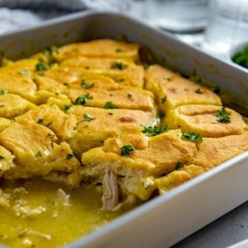 Baked chicken cobbler in a square casserole dish with one serving removed.