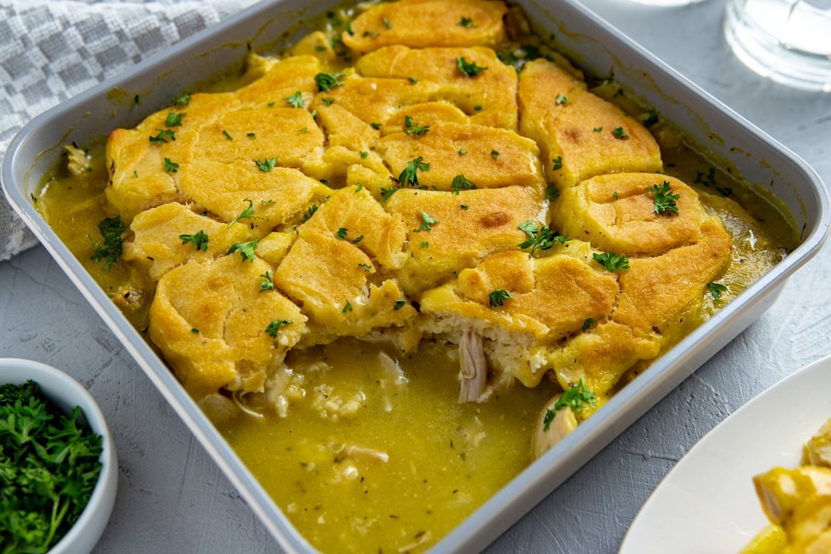 Baked chicken cobbler in a square dish with one serving removed to reveal the inside. Garnished with fresh parsley.