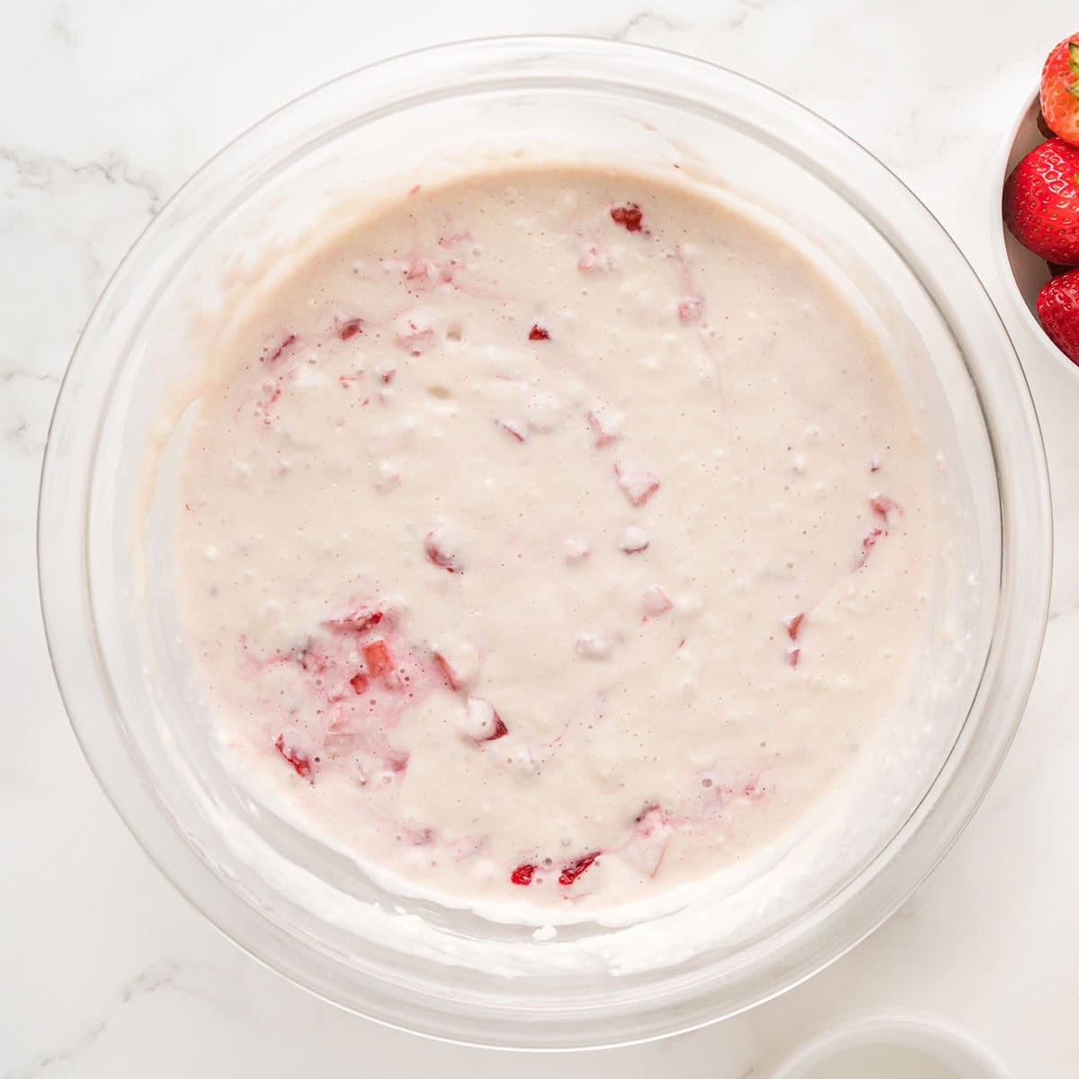 Fresh diced strawberries added to the pancake batter in the glass bowl.