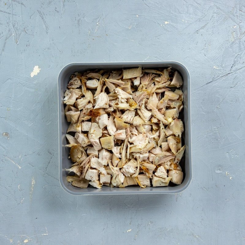 Shredded chicken in the bottom of a square pan.