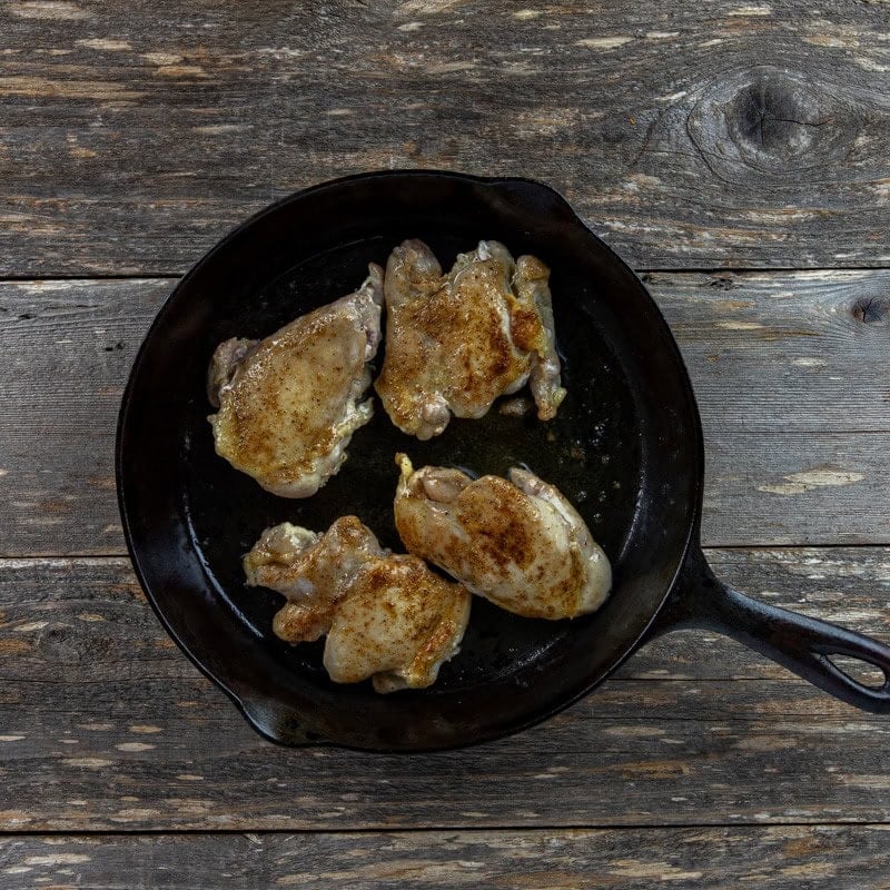 Four browned chicken thighs in a cast iron skillet.
