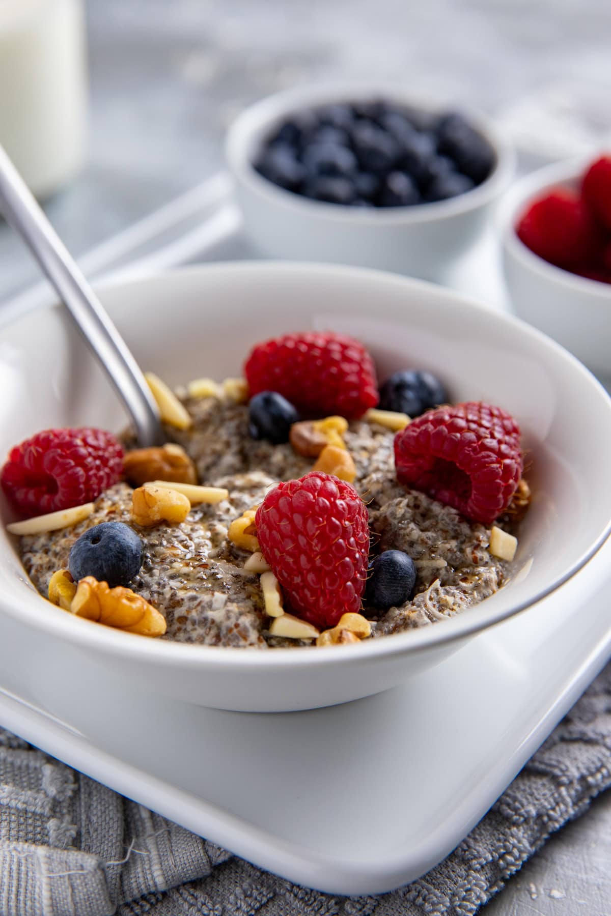 Warm Chia Breakfast Bowl with Berries & Nuts in a white bowl on a white platter with a spoon inside the bowl.