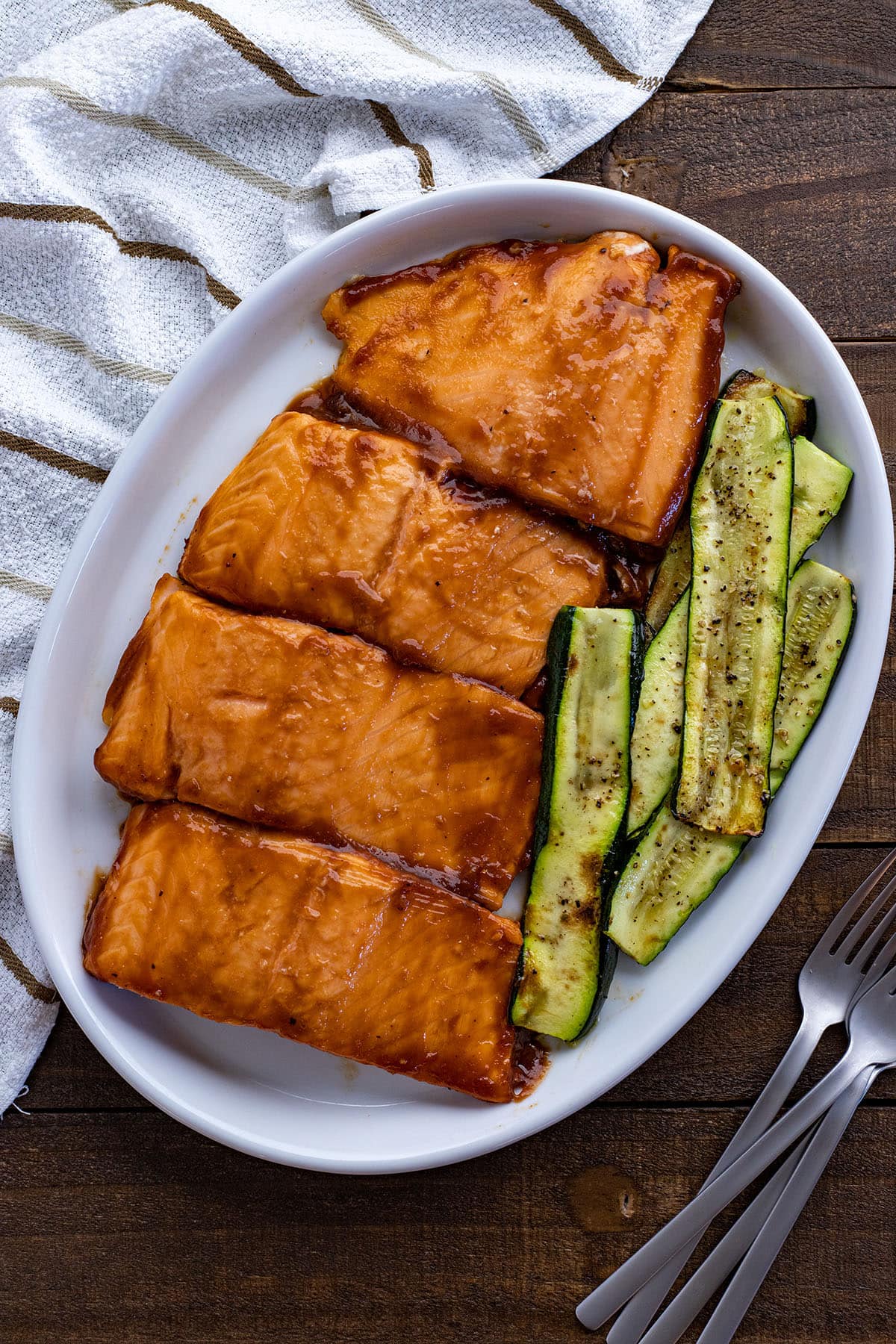 Four grilled salmon fillets brushed with the doctored up BBQ sauce. Grilled zucchini slices next to the salmon. All on a white serving platter.
