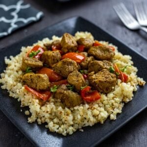 Cooked and cubed pork curry over steamed cauliflower rice on a square black plate.