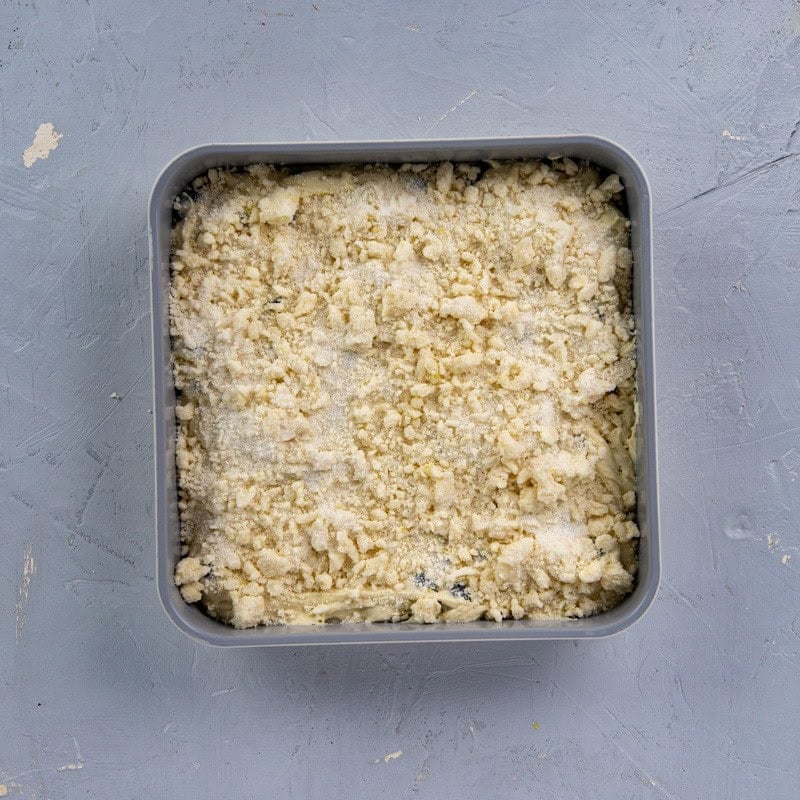 Lemon crumb topping on top of the batter in a square baking pan.