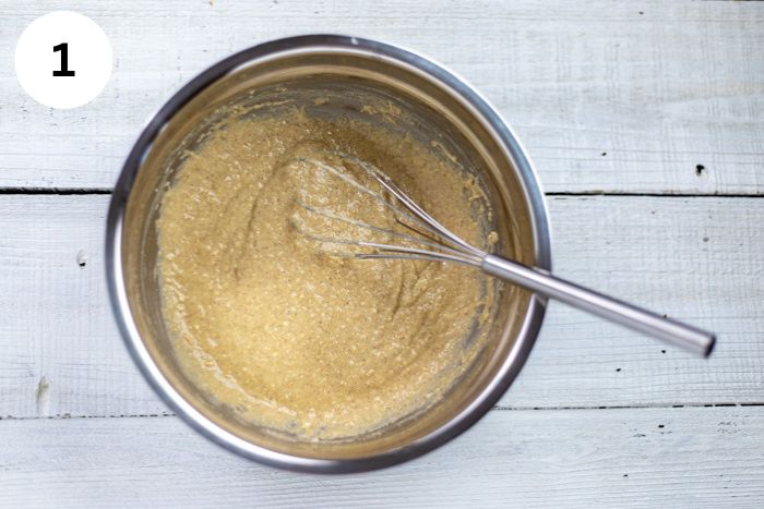 Muffin batter in a steel mixing bowl with wire whisk in the batter.
