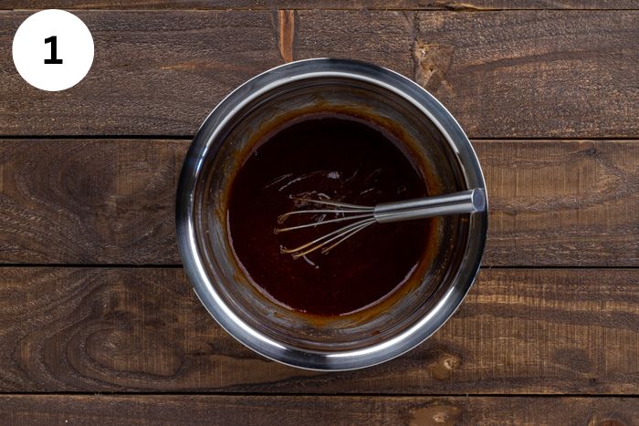 BBQ sauce and other seasonings added to a mixing bowl with a whisk.