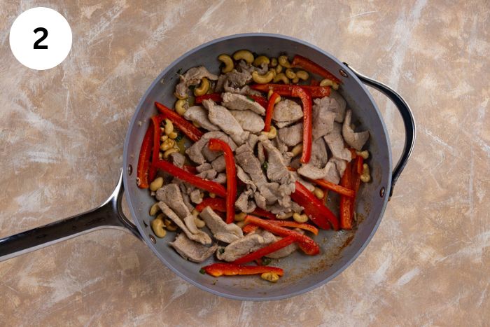 Sliced bell pepper, green onion, ginger, garlic powder, and cashews added to the pork in the skillet.