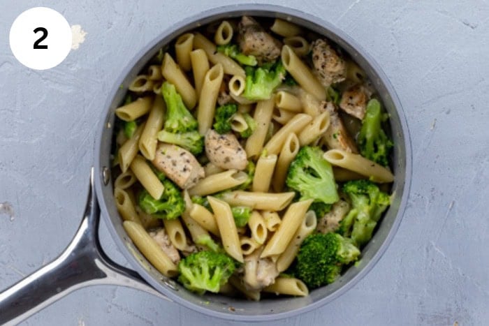 Cooked chicken, steamed broccoli, and cooked penne pasta added to the alfredo sauce in the skillet.