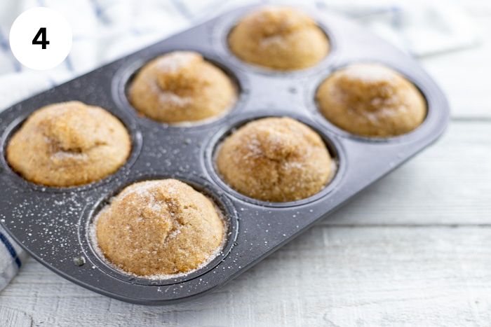 Six baked muffins topping with cinnamon sugar in the muffin pan.