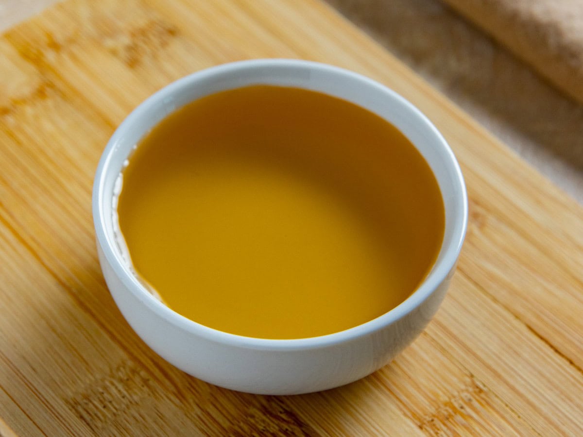 Agave nectar in a small white bowl on a wooden cutting board.