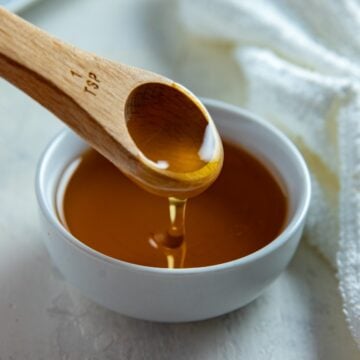 Honey in a small white bowl with a wooden spoon dipping in.