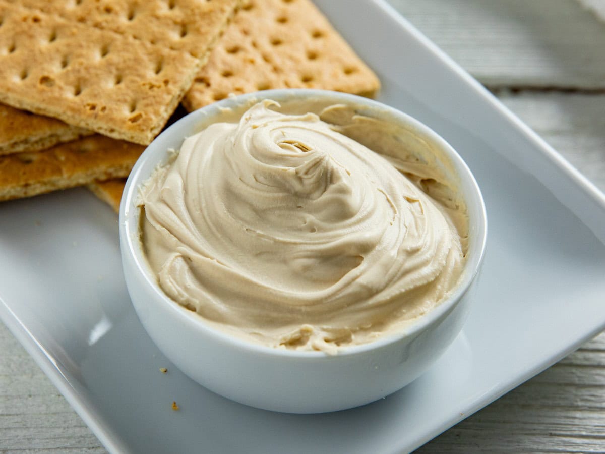 Mascarpone cheese in a small white bowl with graham crackers in the background.