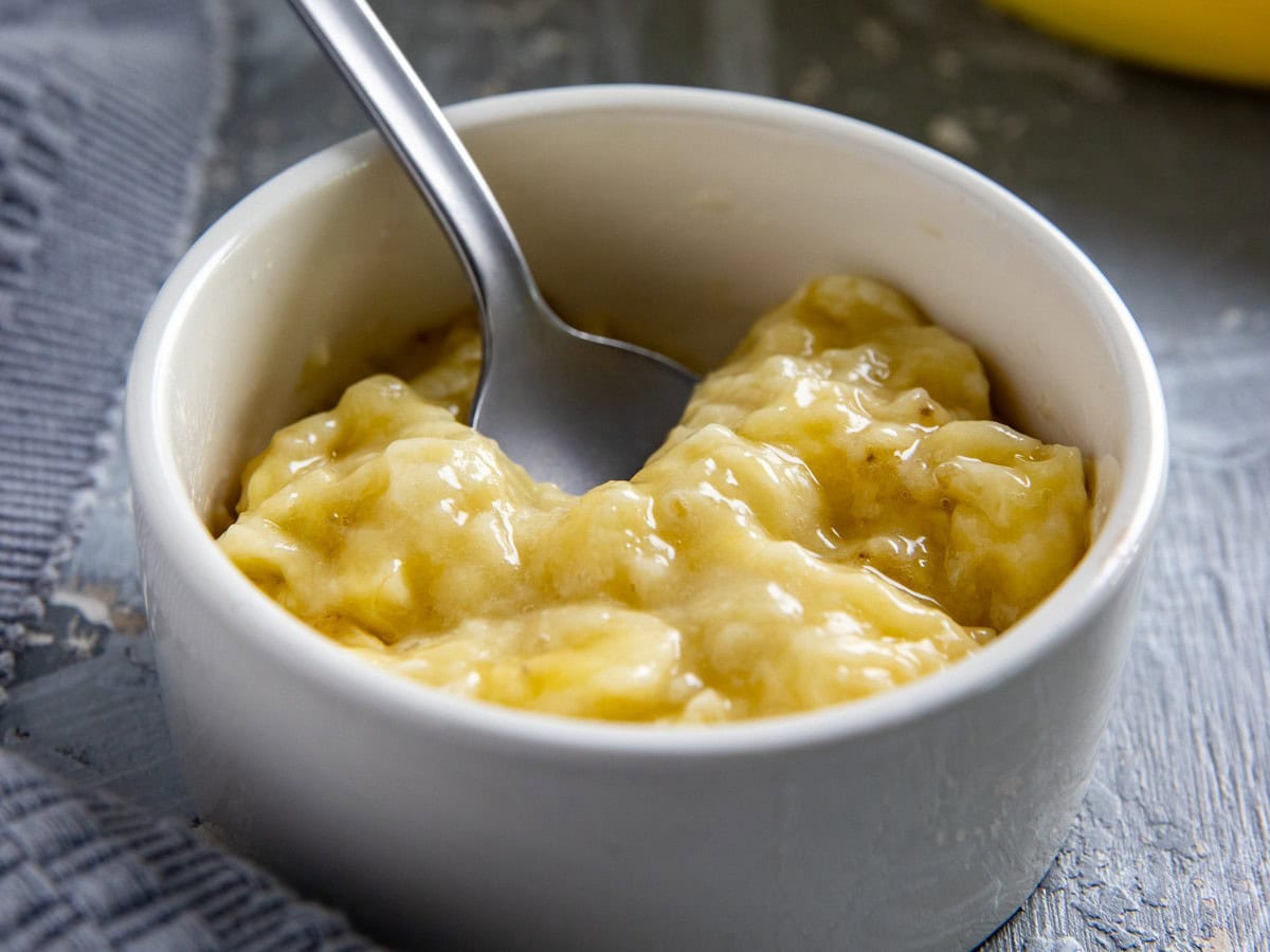 Mashed banana in a small white bowl with a spoon in it.