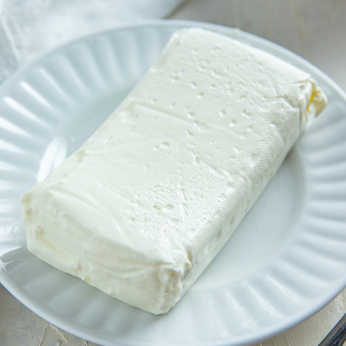 A block of Neufchatel cheese on a white plate.