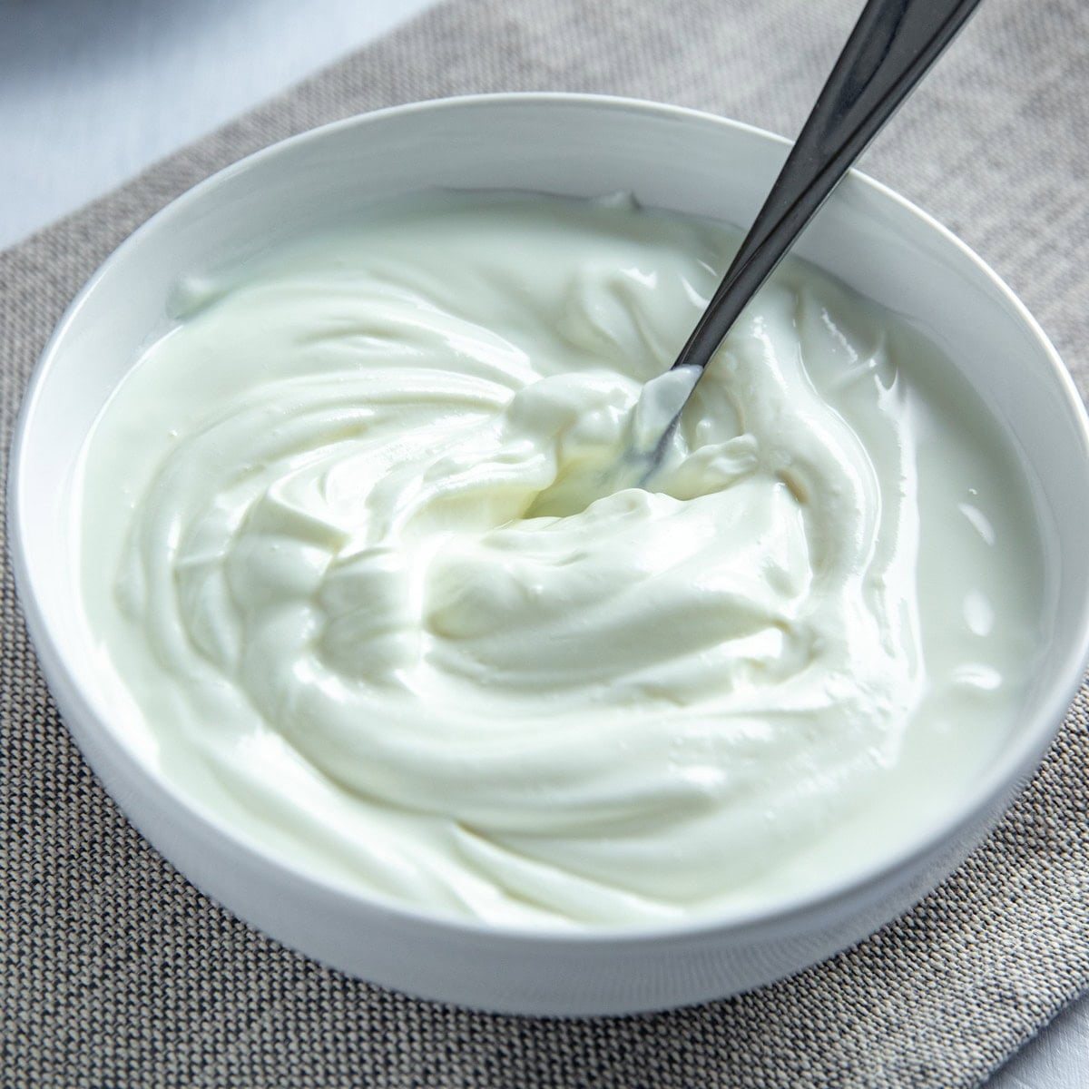 Plain greek yogurt in a small white bowl with spoon inside.