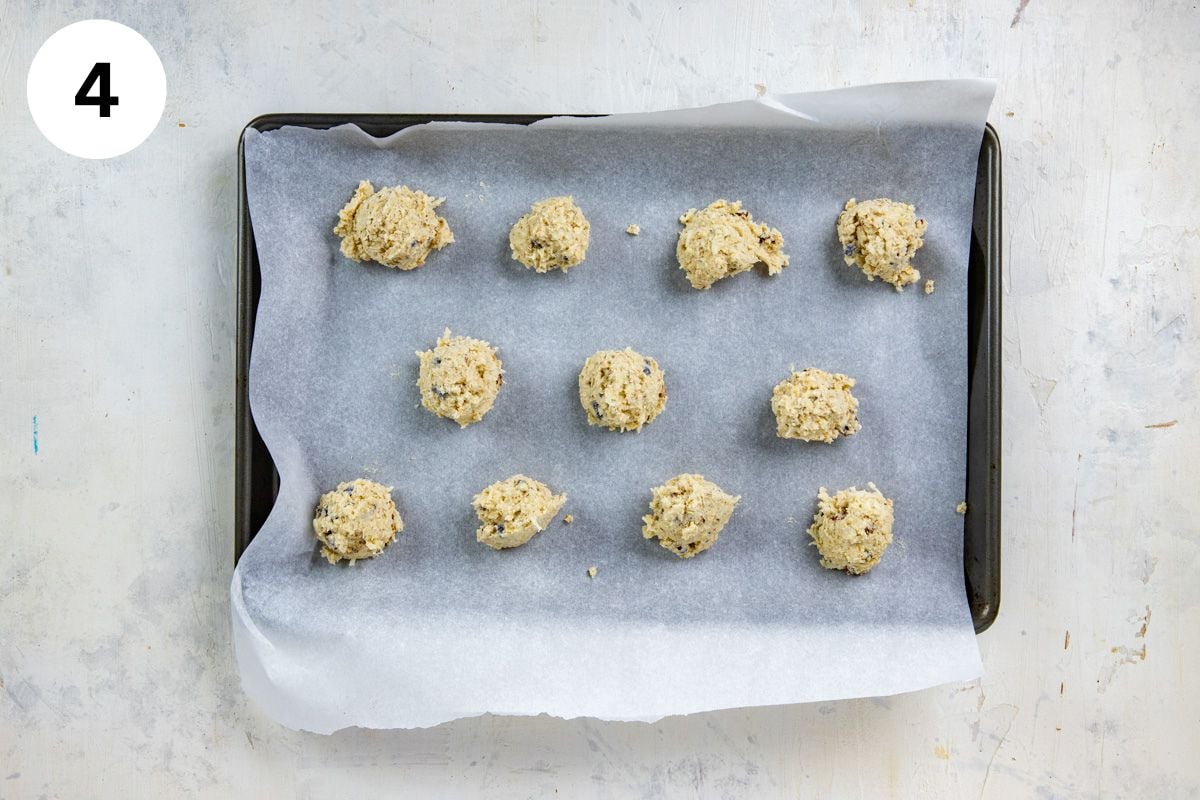 Eleven scoops of cookie dough on parchment paper on cookie sheet.