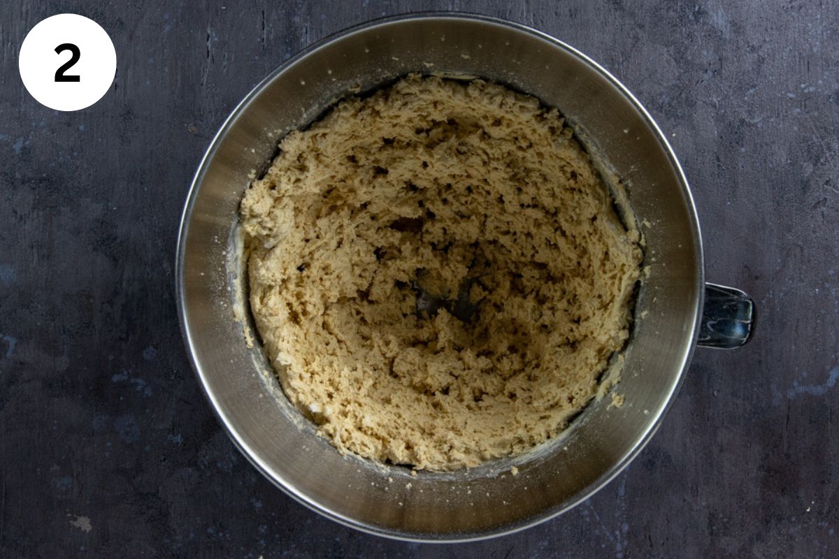Vanilla and almond extracts and eggs blended in with the butter-sugar mixture in a stainless steel mixing bowl.