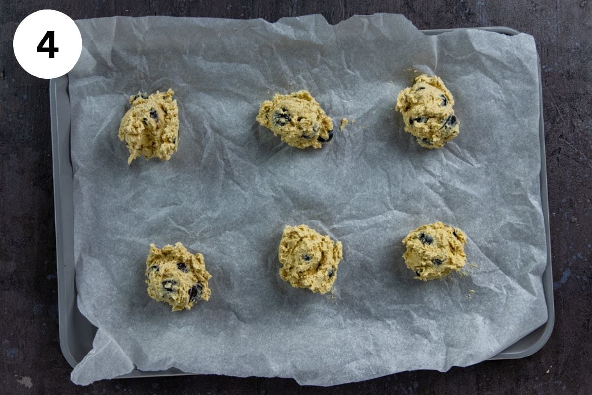 Scoops of raw cookie dough on parchment paper-lined cookie sheet.