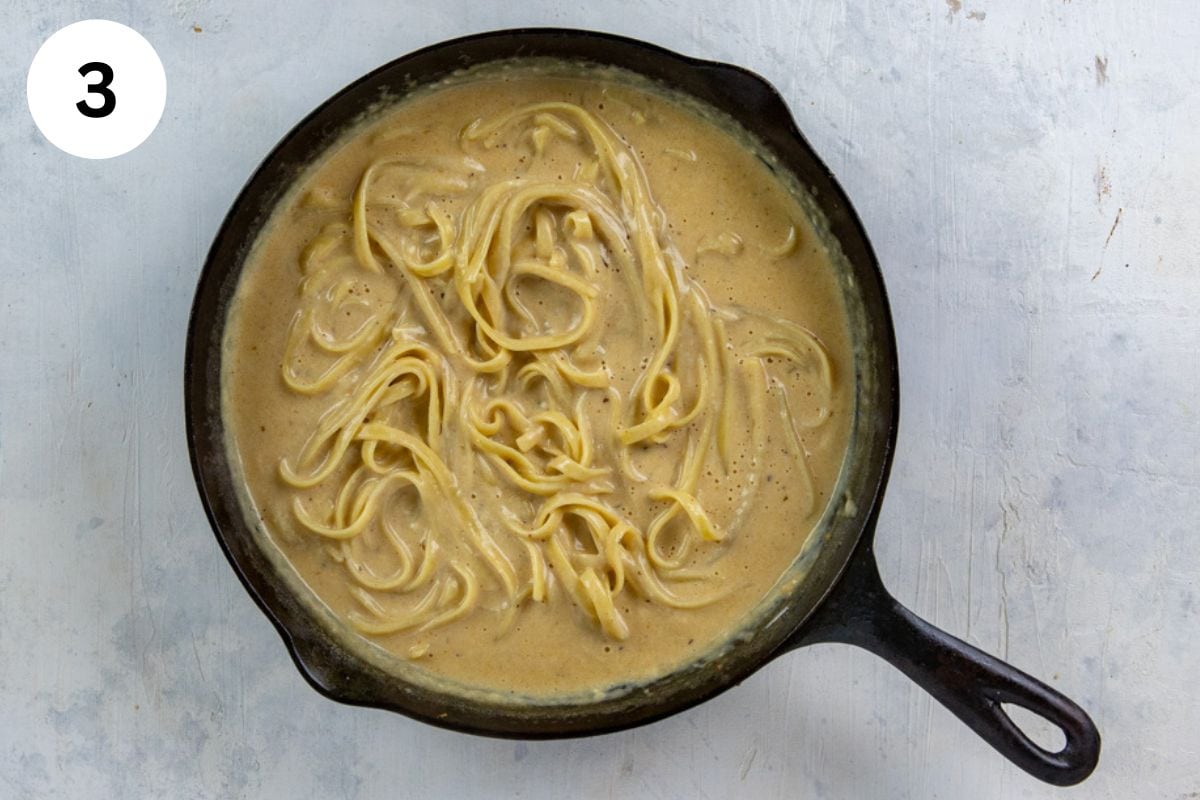 Cooked pasta mixed in with the alfredo sauce in a cast iron skillet.