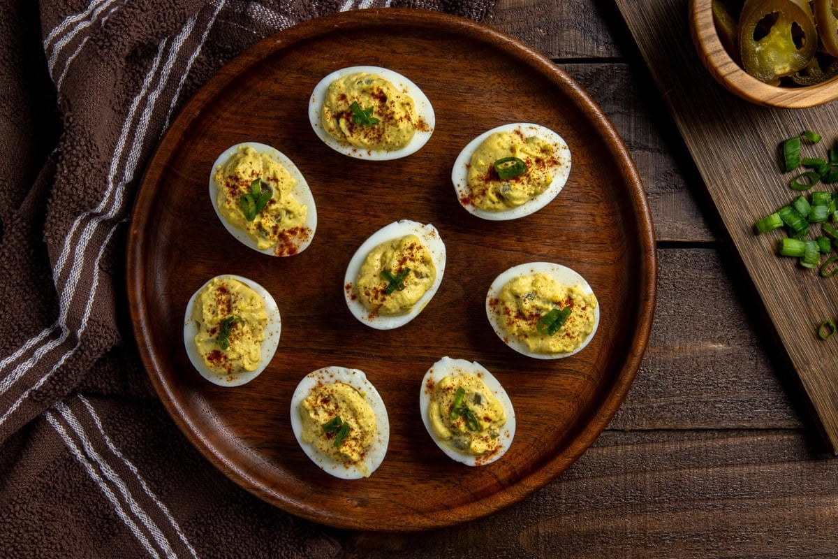 Overhead view of 8 deviled eggs on round wooden serving platter.