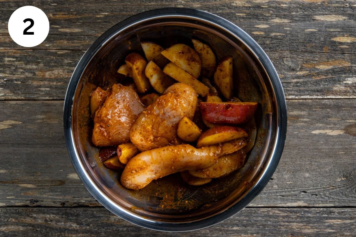 Uncooked chicken and potatoes in a bowl with the cajun butter sauce.
