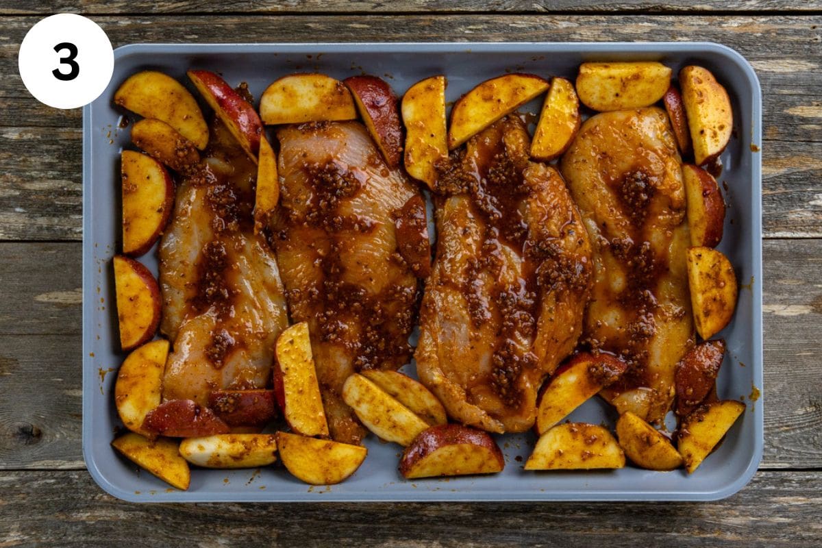 Uncooked seasoned chicken and potato wedges on a sheet pan.