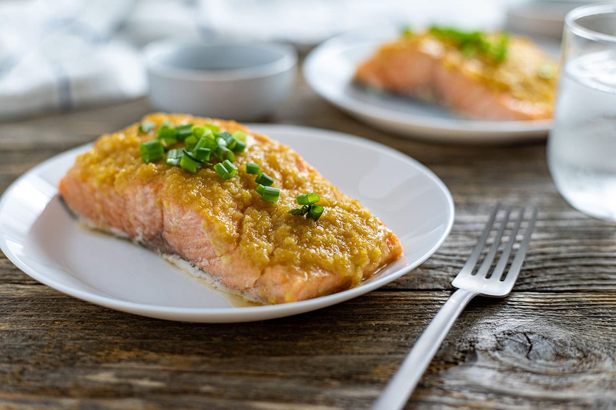 Cooked salmon fillets topped with reserved miso marinade on a white plate with a fork and glass of water in the background.
