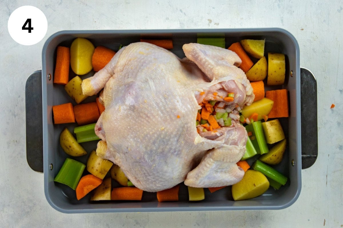 Whole raw chicken stuffed with small-chopped vegetables placed inside the chicken cavity and the larger chopped vegetables on a sheet pan.